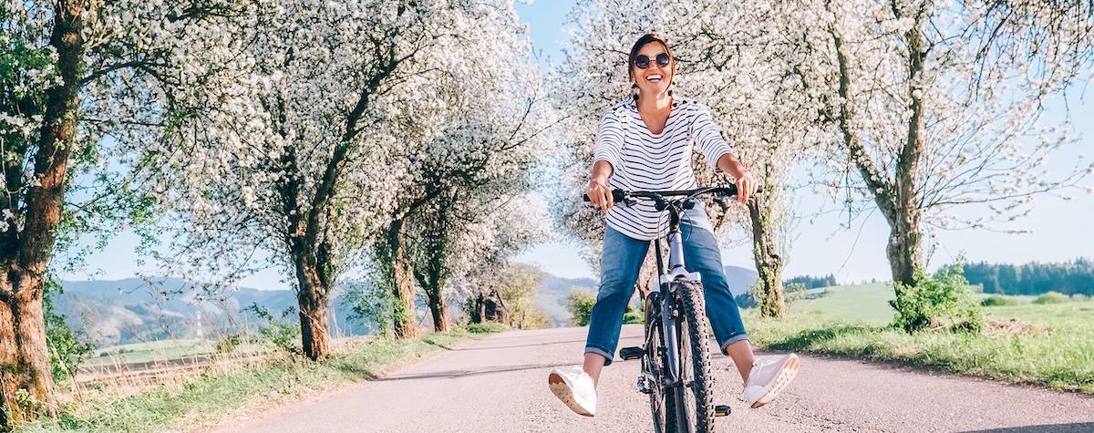 Happy smiling woman rides a bicycle on the country road under the apple blossom trees