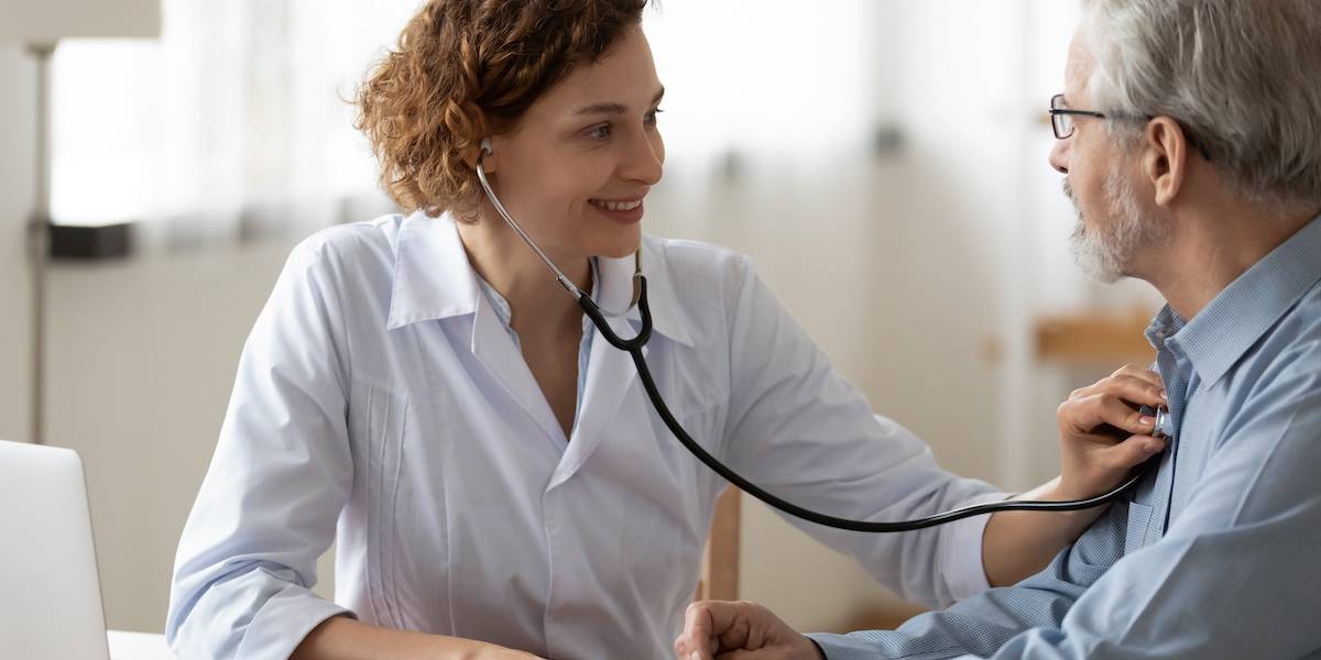 Smiling young woman nurse using stethoscope, checking mature patient