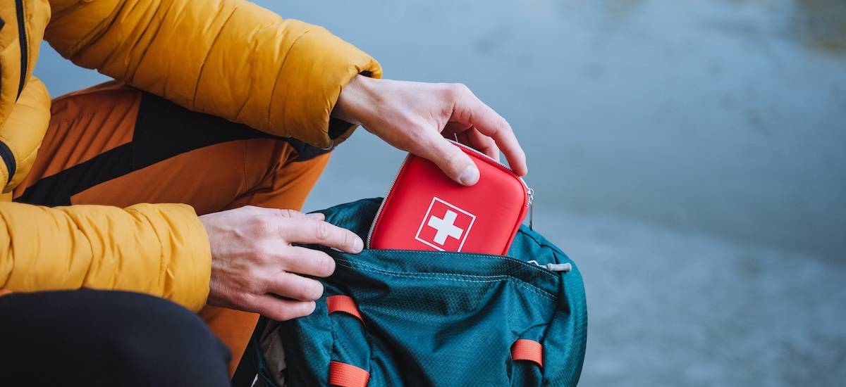 A guy puts a first aid kit in a backpack, packing things for a hike, safety in a winter trip, trekking in the mountains. personal first aid kit.