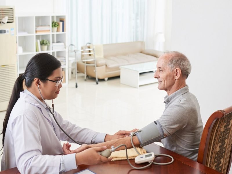 Asian female doctor measuring patient blood pressure during Medicare home care visit
