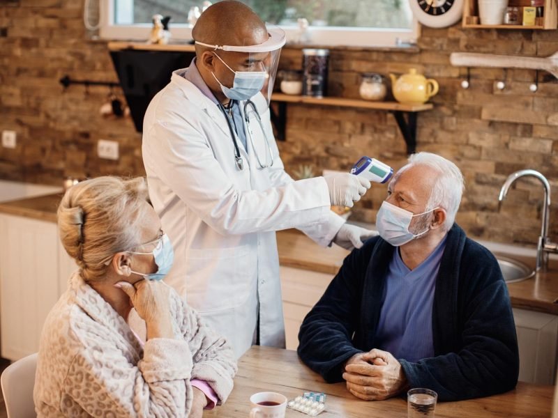 Senior couple having temperature measured by doctor during Medicare home visit consultation
