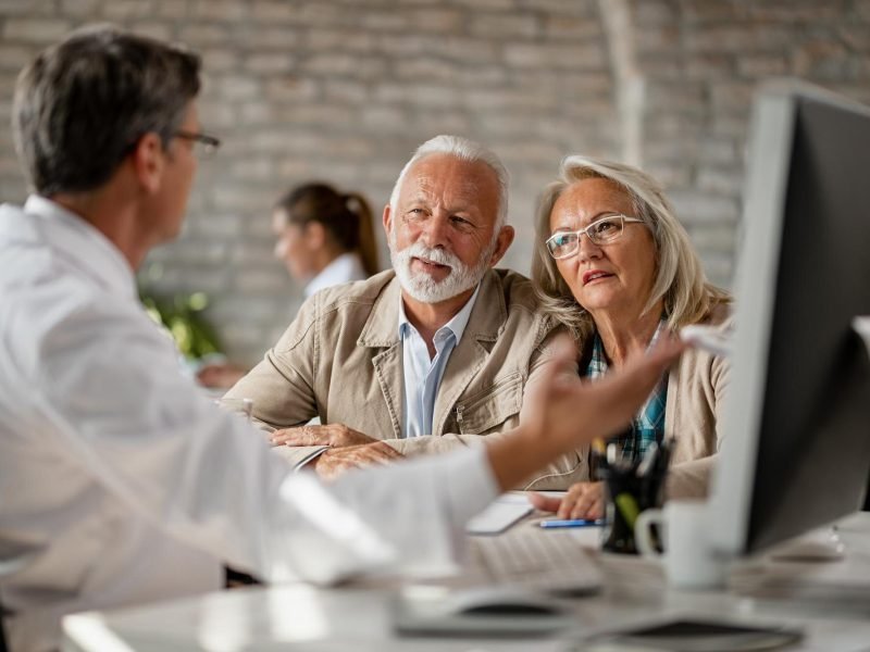 Senior couple talking with doctor about Medicare medical records during clinic consultation